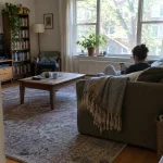 Person sitter avslappnat i soffan och kollar iPhone, tips för att blockera tidskrävande appar med Skärmtid.